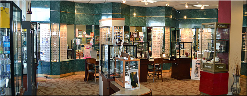 A wide interior shot of the entire Optima Optometry designer eyewear boutique showroom in Santa Clara, featuring marble accents, extensive display cases, rich wood paneling, and a distinct Cartier brand kiosk.