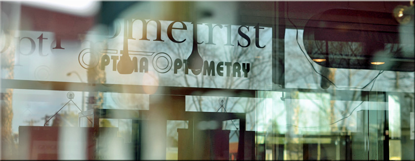 The glass storefront window of Optima Optometry in Santa Clara showing the black vinyl logo and text that reads Optometrist Optima Optometry with outdoor reflections.
