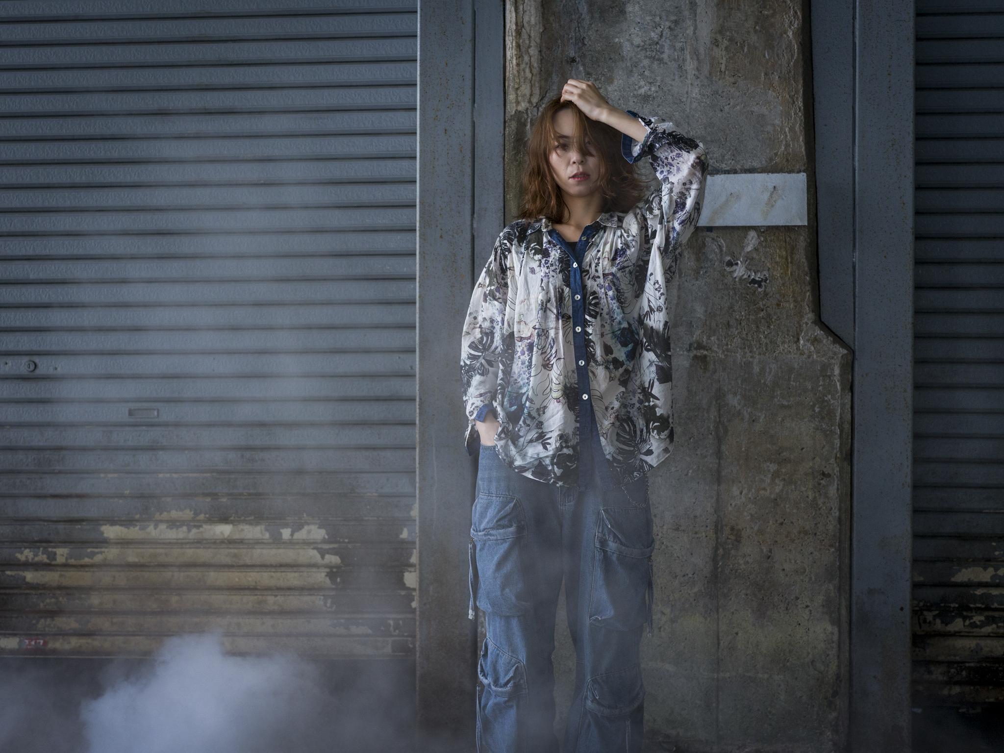 Japanese model Koishi showcasing personal street style wardrobe choices within a moody, industrial urban landscape during a rainy-day fashion editorial around Hankyu Nakatsu Station in Osaka.