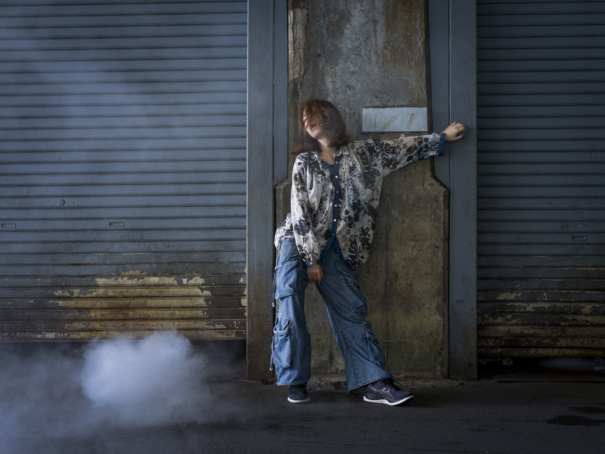 Japanese model Koishi showcasing personal street style wardrobe choices within a moody, industrial urban landscape during a rainy-day fashion editorial around Hankyu Nakatsu Station in Osaka.
