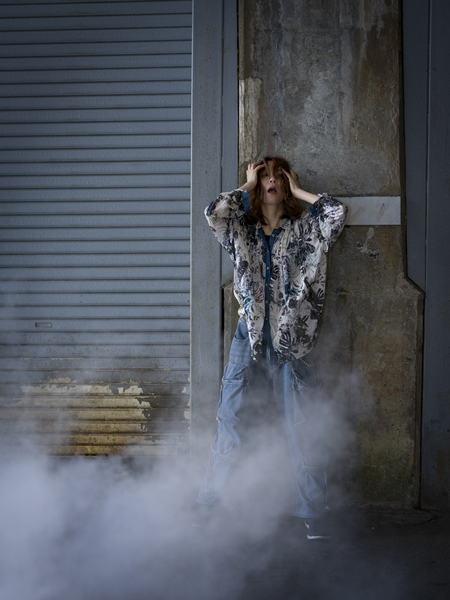 Japanese model Koishi showcasing personal street style wardrobe choices within a moody, industrial urban landscape during a rainy-day fashion editorial around Hankyu Nakatsu Station in Osaka.