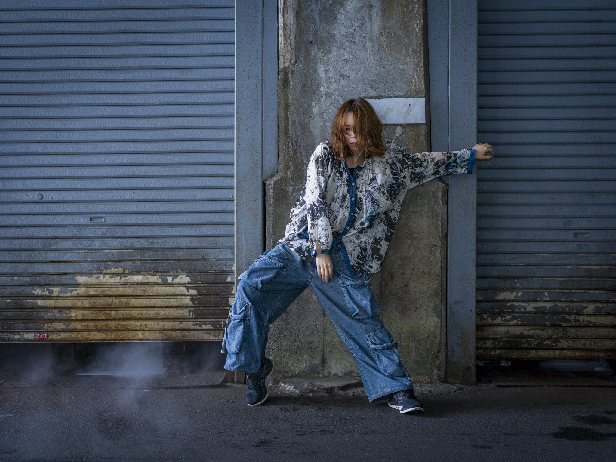 Japanese model Koishi showcasing personal street style wardrobe choices within a moody, industrial urban landscape during a rainy-day fashion editorial around Hankyu Nakatsu Station in Osaka.