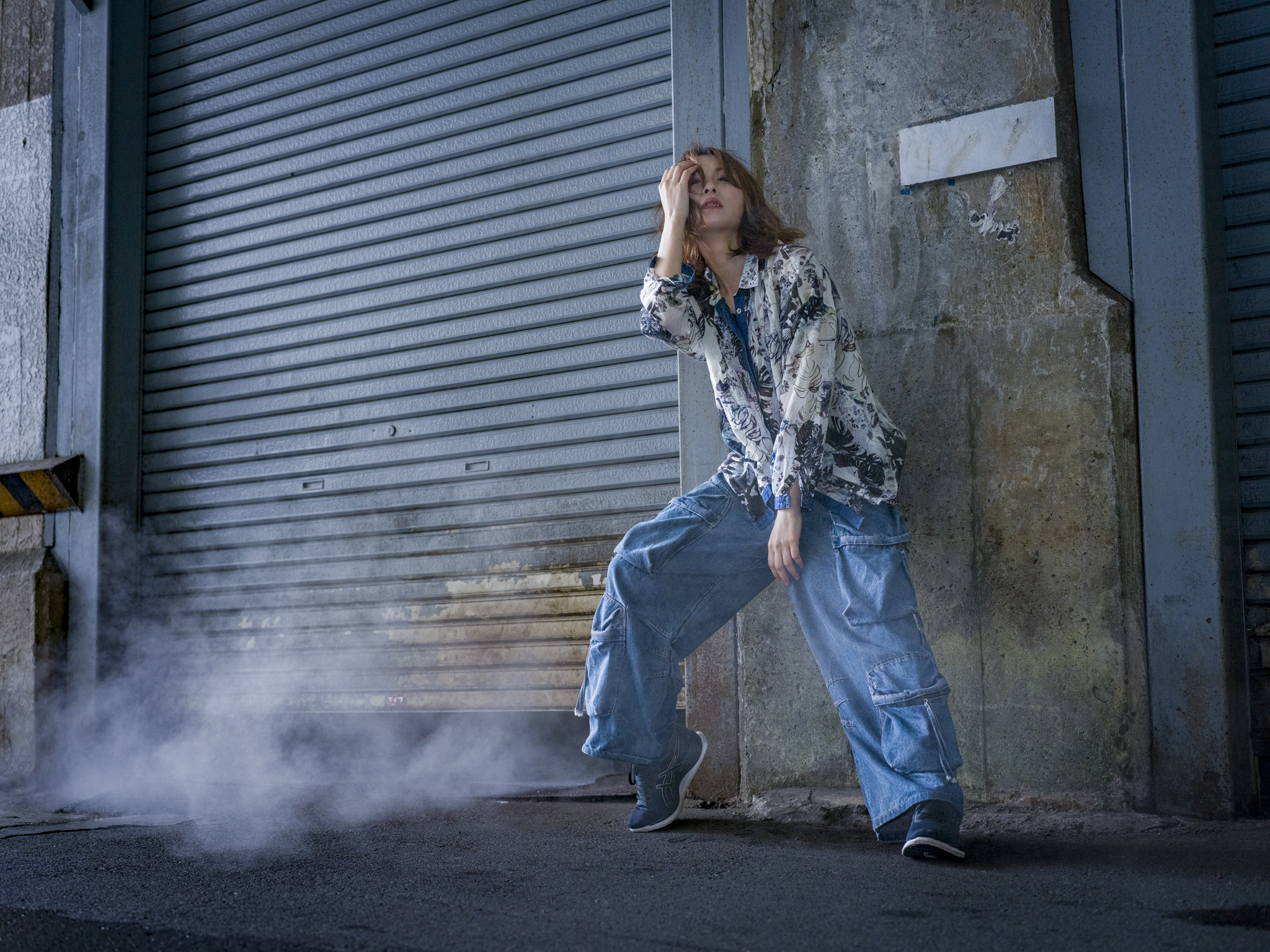 Japanese model Koishi showcasing personal street style wardrobe choices within a moody, industrial urban landscape during a rainy-day fashion editorial around Hankyu Nakatsu Station in Osaka.