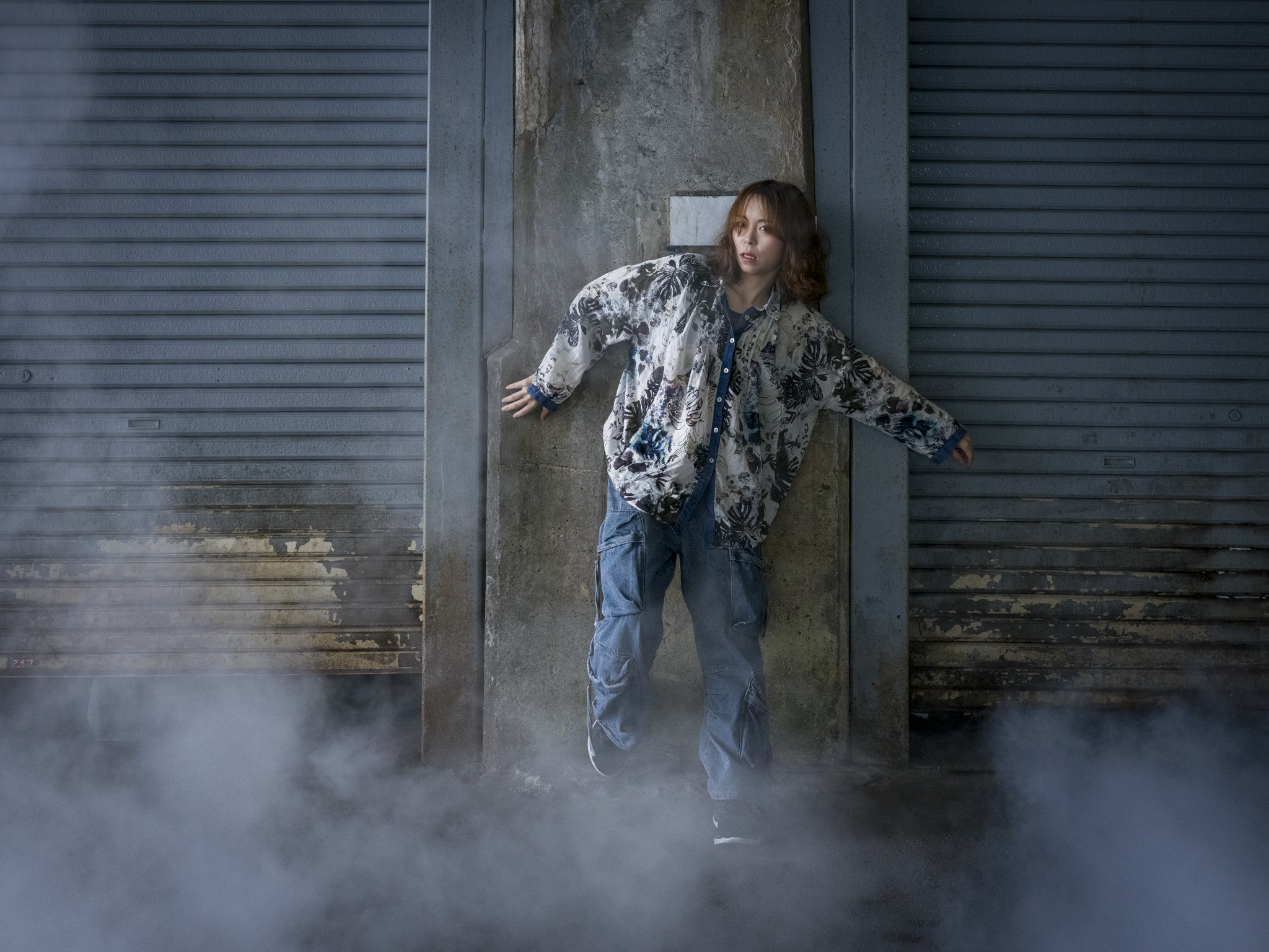 Japanese model Koishi showcasing personal street style wardrobe choices within a moody, industrial urban landscape during a rainy-day fashion editorial around Hankyu Nakatsu Station in Osaka.