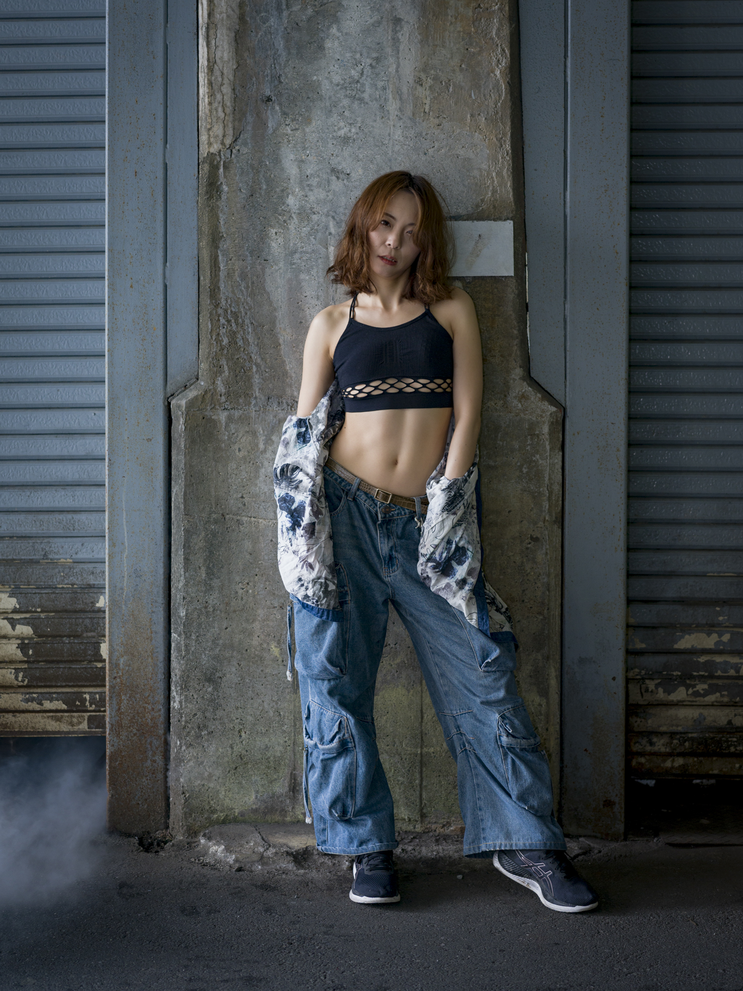 Japanese model Koishi showcasing personal street style wardrobe choices within a moody, industrial urban landscape during a rainy-day fashion editorial around Hankyu Nakatsu Station in Osaka.