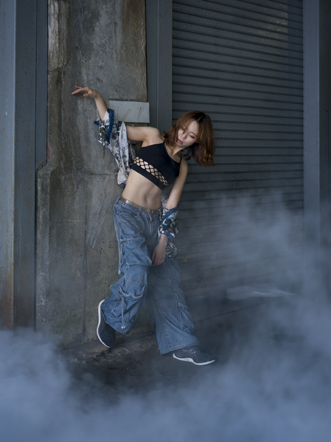 Japanese model Koishi showcasing personal street style wardrobe choices within a moody, industrial urban landscape during a rainy-day fashion editorial around Hankyu Nakatsu Station in Osaka.