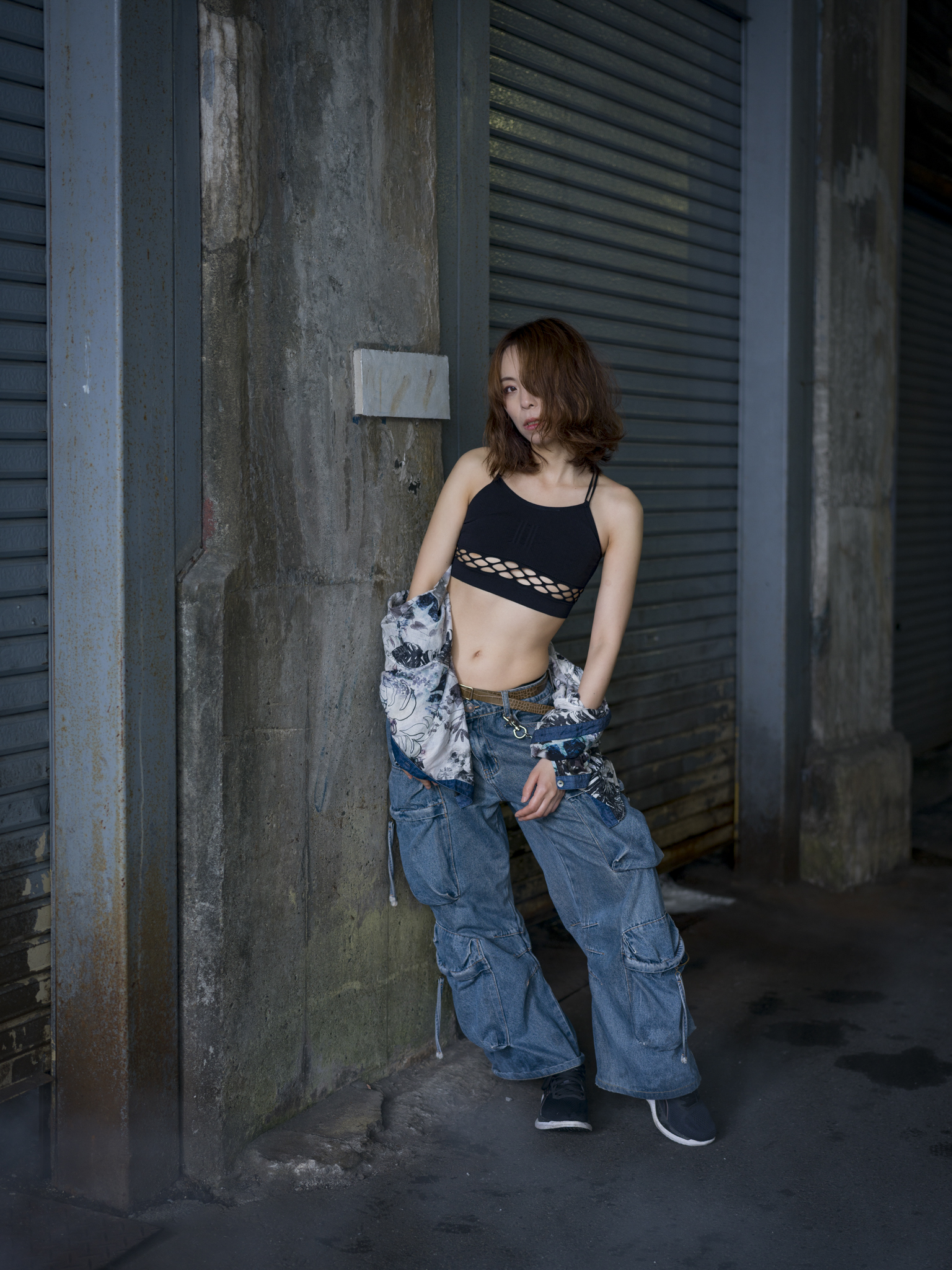 Japanese model Koishi showcasing personal street style wardrobe choices within a moody, industrial urban landscape during a rainy-day fashion editorial around Hankyu Nakatsu Station in Osaka.