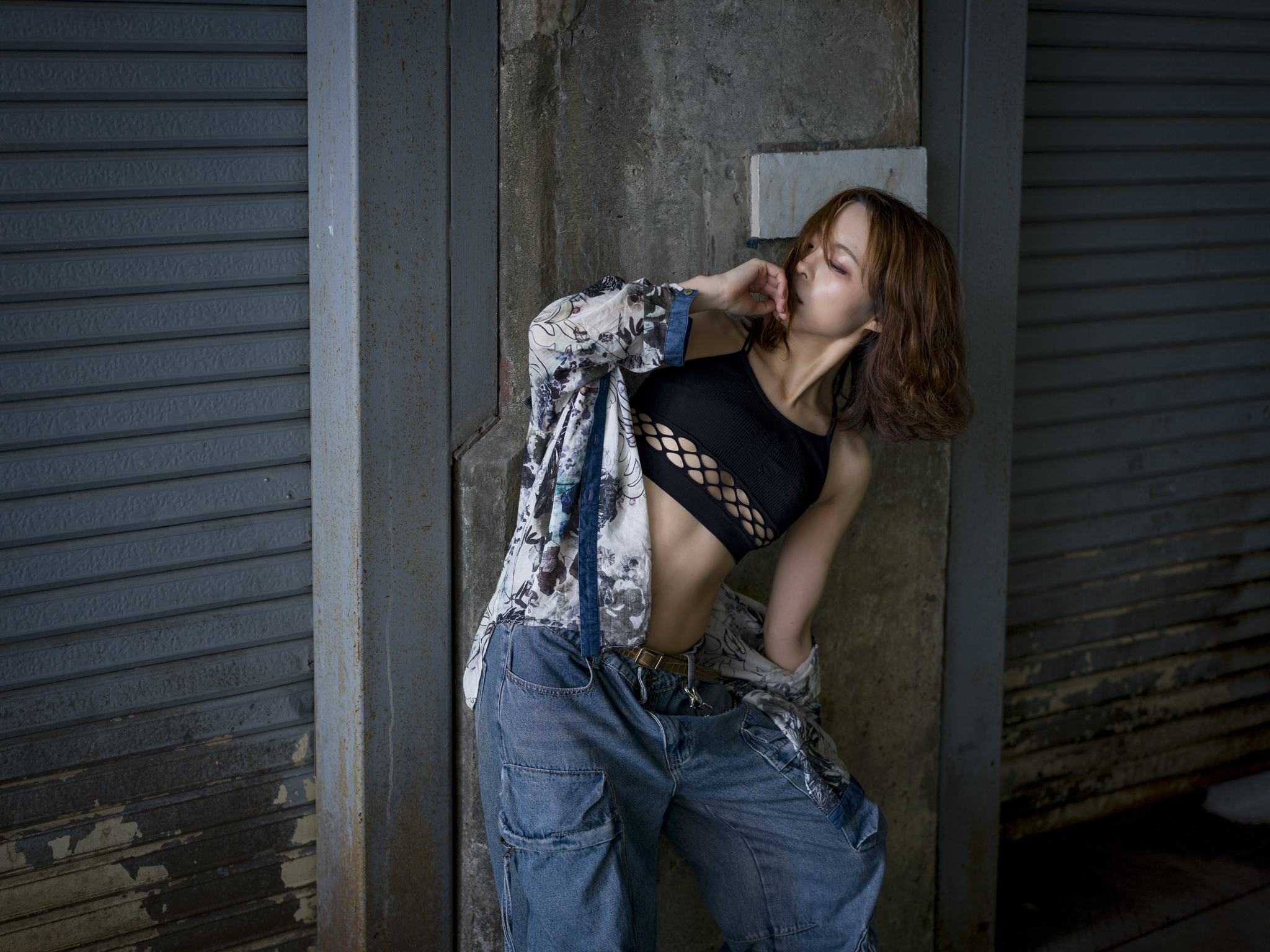 Japanese model Koishi showcasing personal street style wardrobe choices within a moody, industrial urban landscape during a rainy-day fashion editorial around Hankyu Nakatsu Station in Osaka.