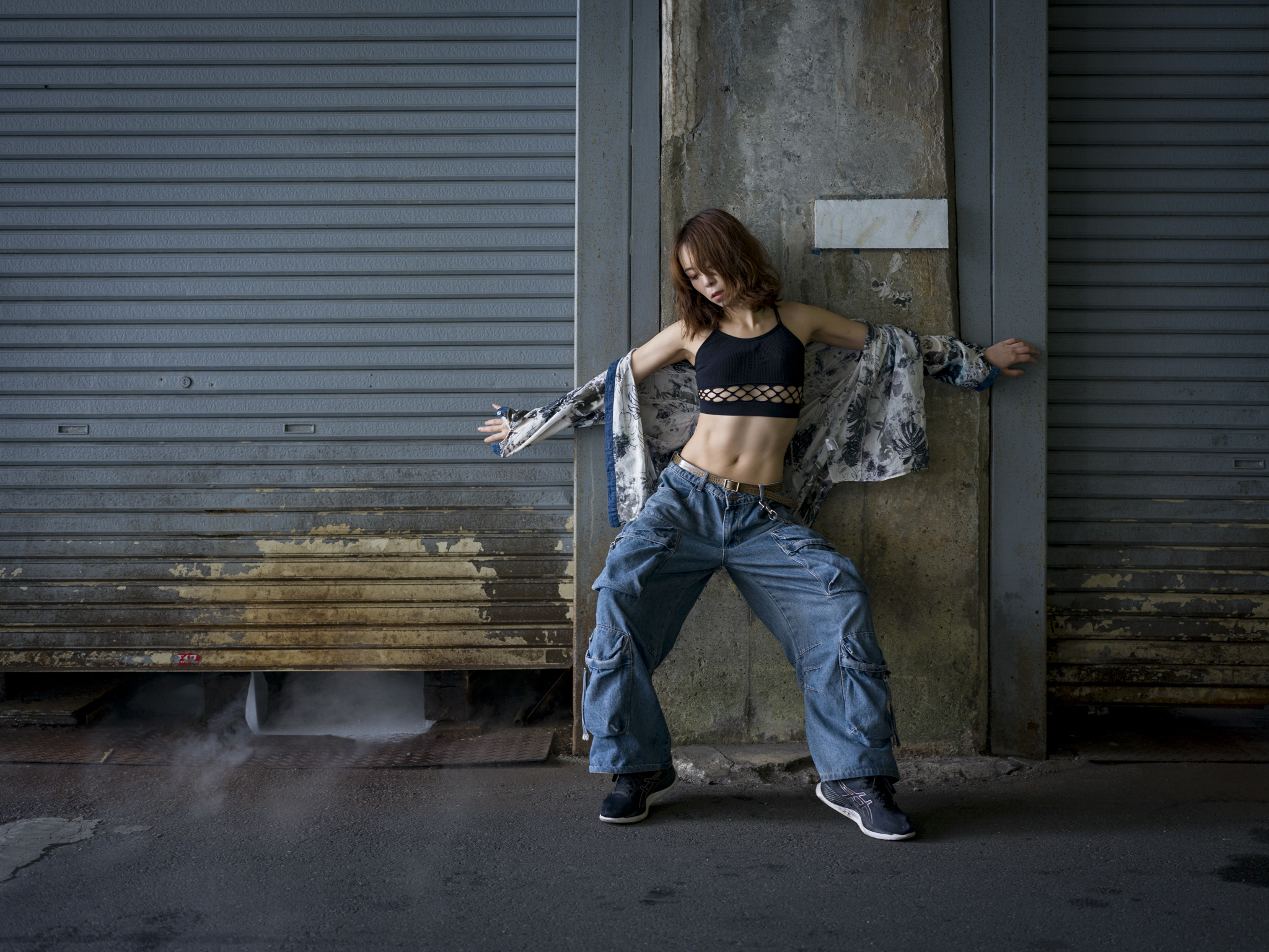 Japanese model Koishi showcasing personal street style wardrobe choices within a moody, industrial urban landscape during a rainy-day fashion editorial around Hankyu Nakatsu Station in Osaka.