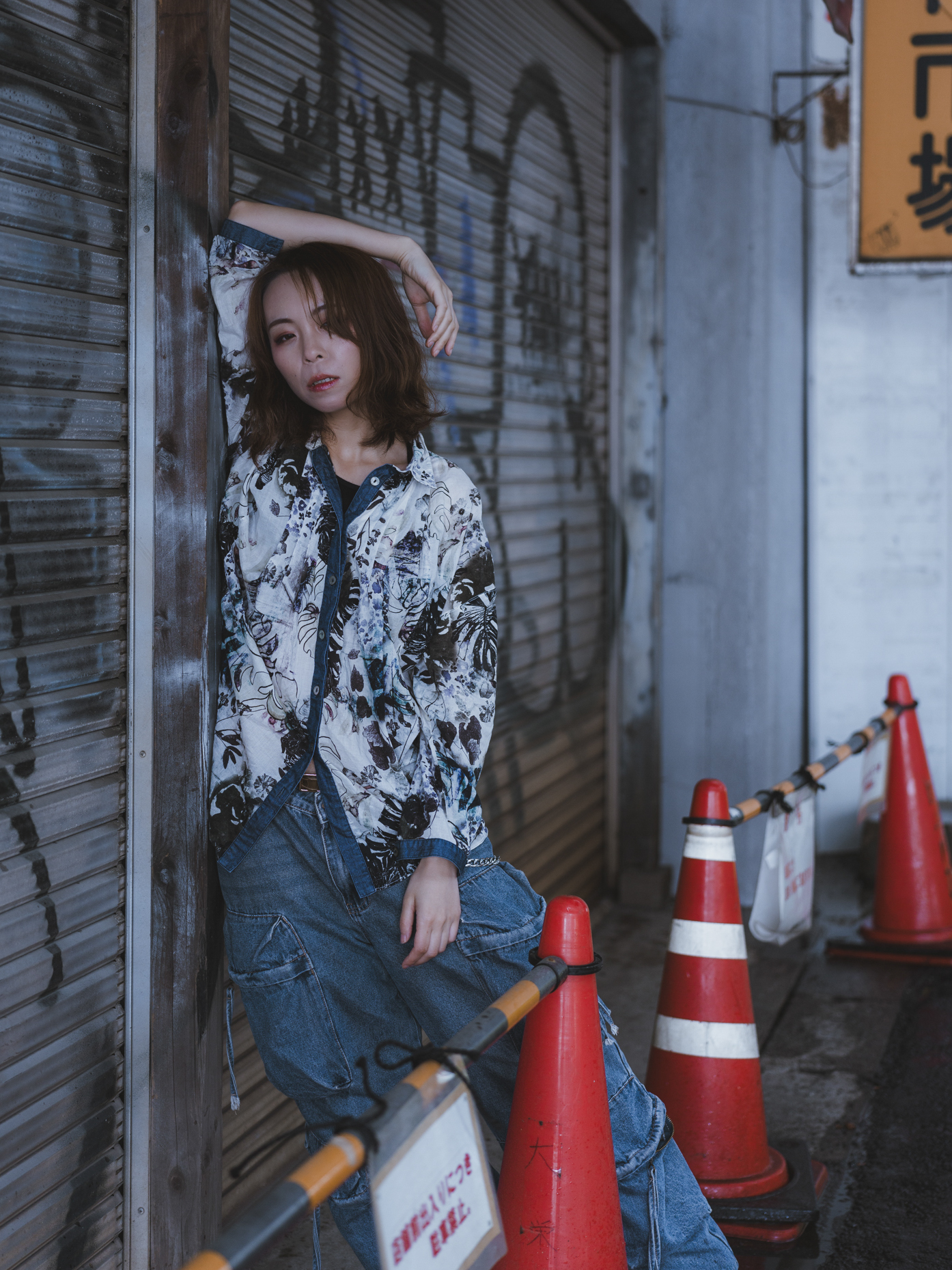 Japanese model Koishi showcasing personal street style wardrobe choices within a moody, industrial urban landscape during a rainy-day fashion editorial around Hankyu Nakatsu Station in Osaka.