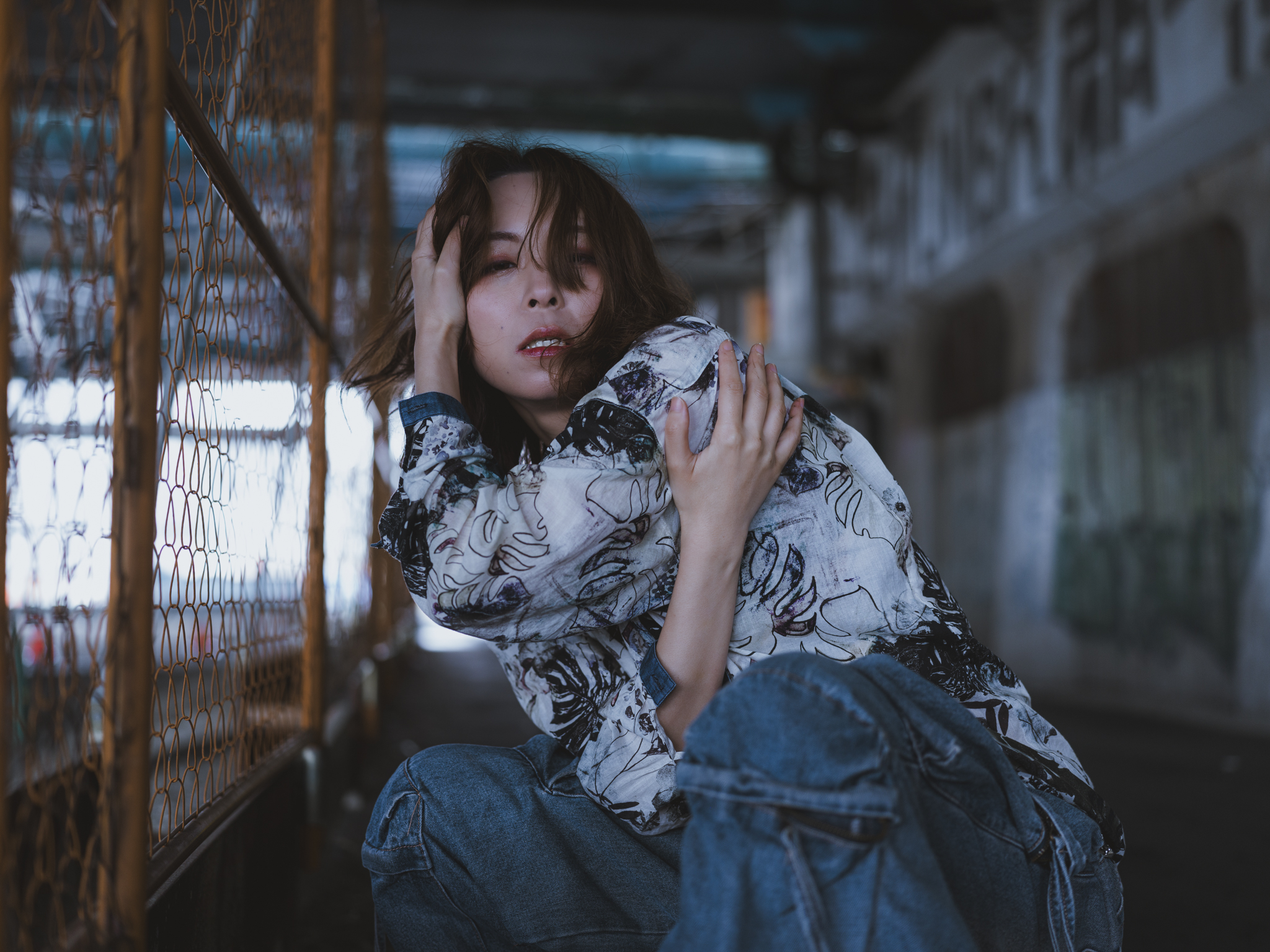 Japanese model Koishi showcasing personal street style wardrobe choices within a moody, industrial urban landscape during a rainy-day fashion editorial around Hankyu Nakatsu Station in Osaka.