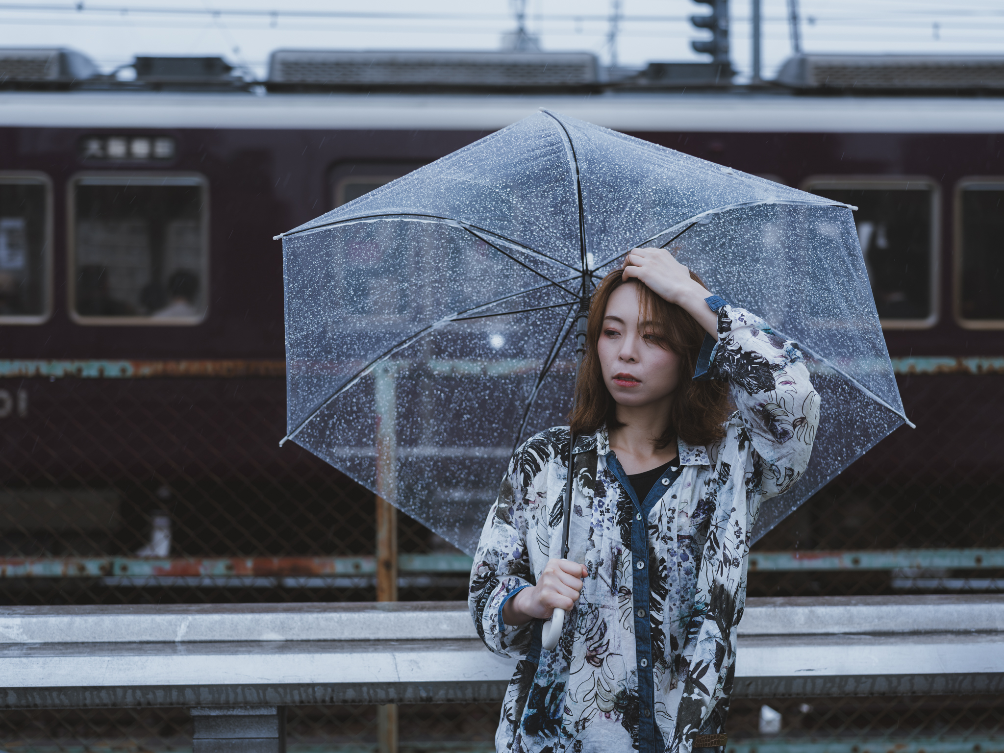 Japanese model Koishi showcasing personal street style wardrobe choices within a moody, industrial urban landscape during a rainy-day fashion editorial around Hankyu Nakatsu Station in Osaka.