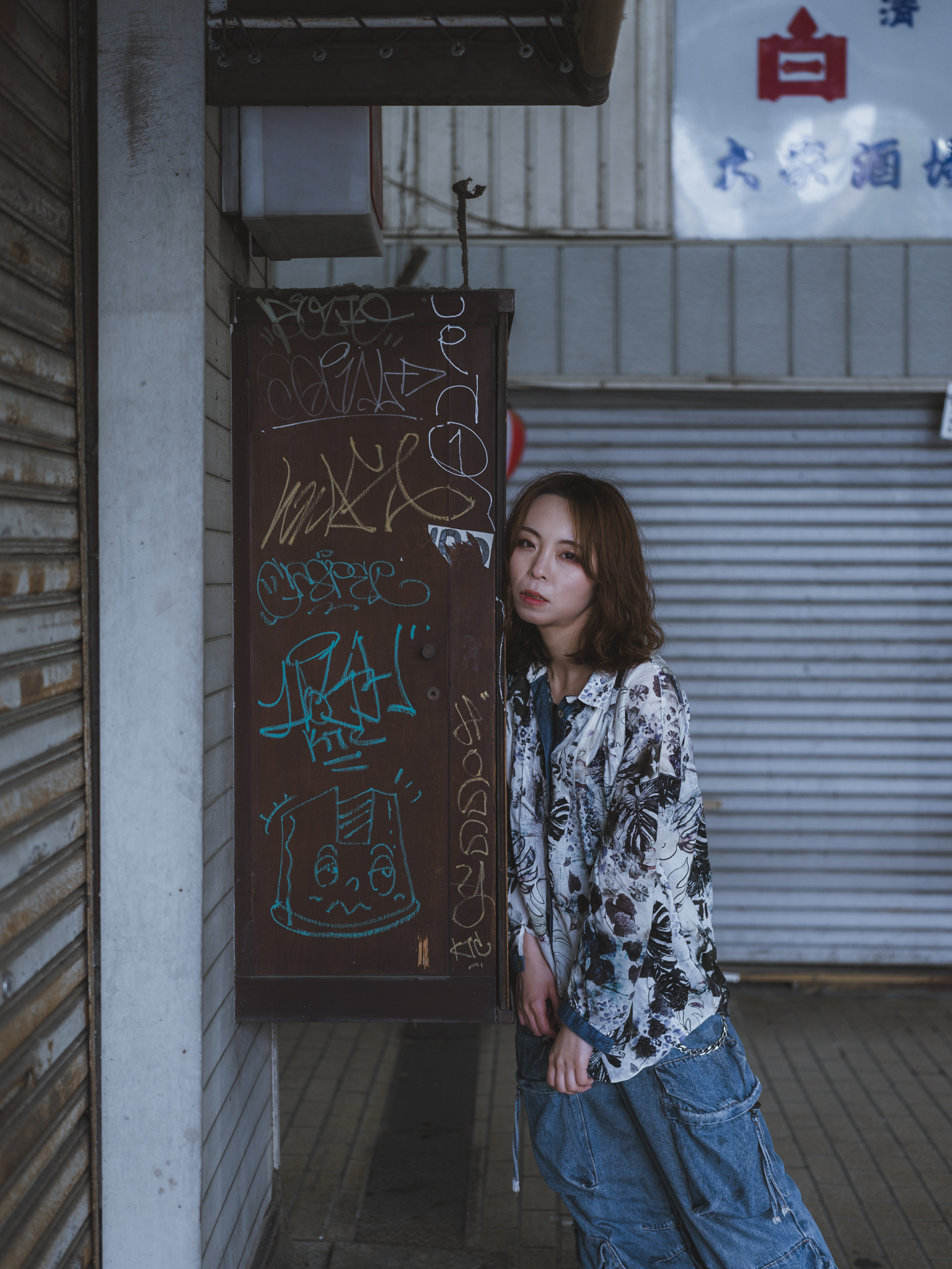 Japanese model Koishi showcasing personal street style wardrobe choices within a moody, industrial urban landscape during a rainy-day fashion editorial around Hankyu Nakatsu Station in Osaka.
