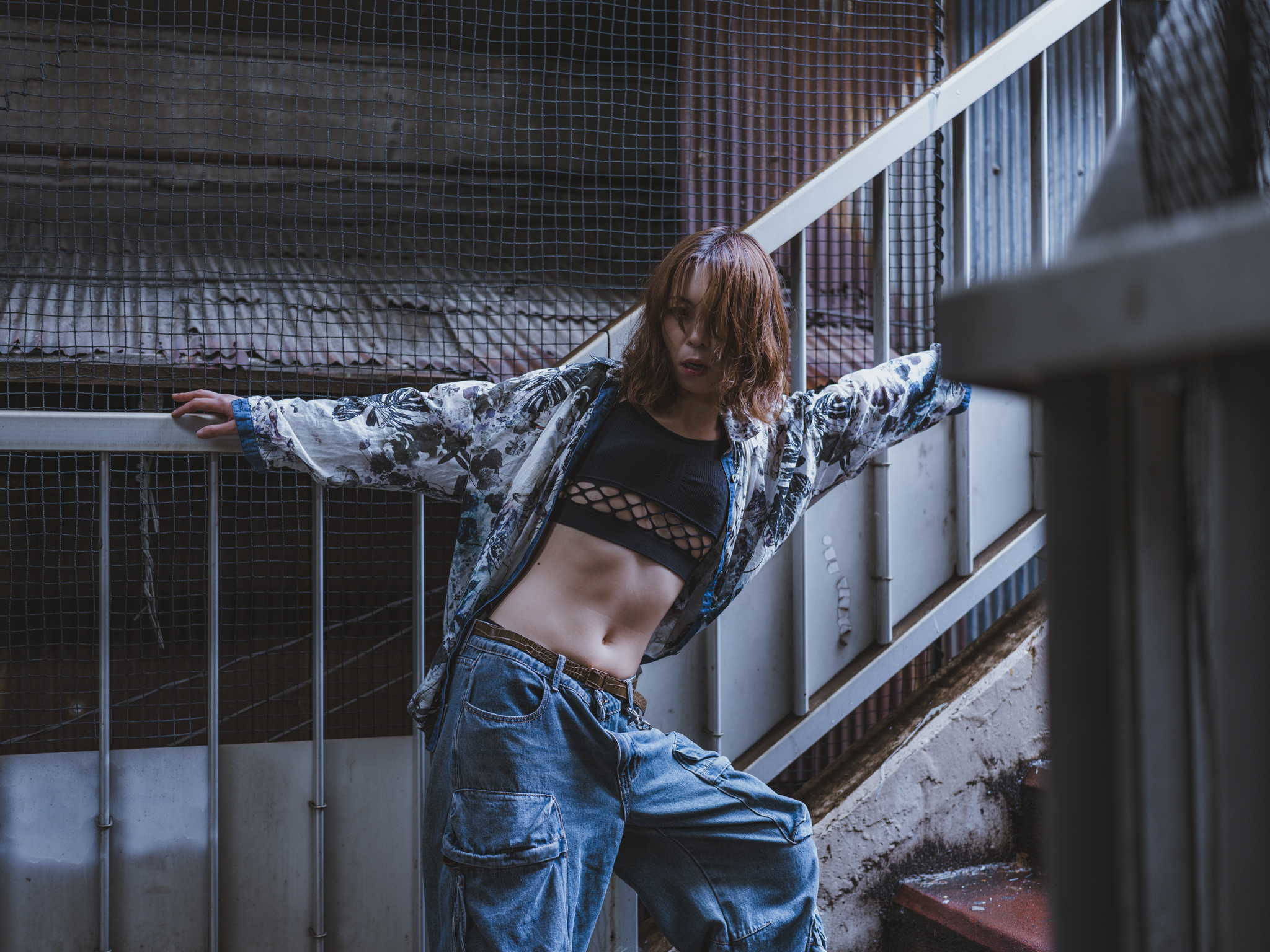 Japanese model Koishi showcasing personal street style wardrobe choices within a moody, industrial urban landscape during a rainy-day fashion editorial around Hankyu Nakatsu Station in Osaka.