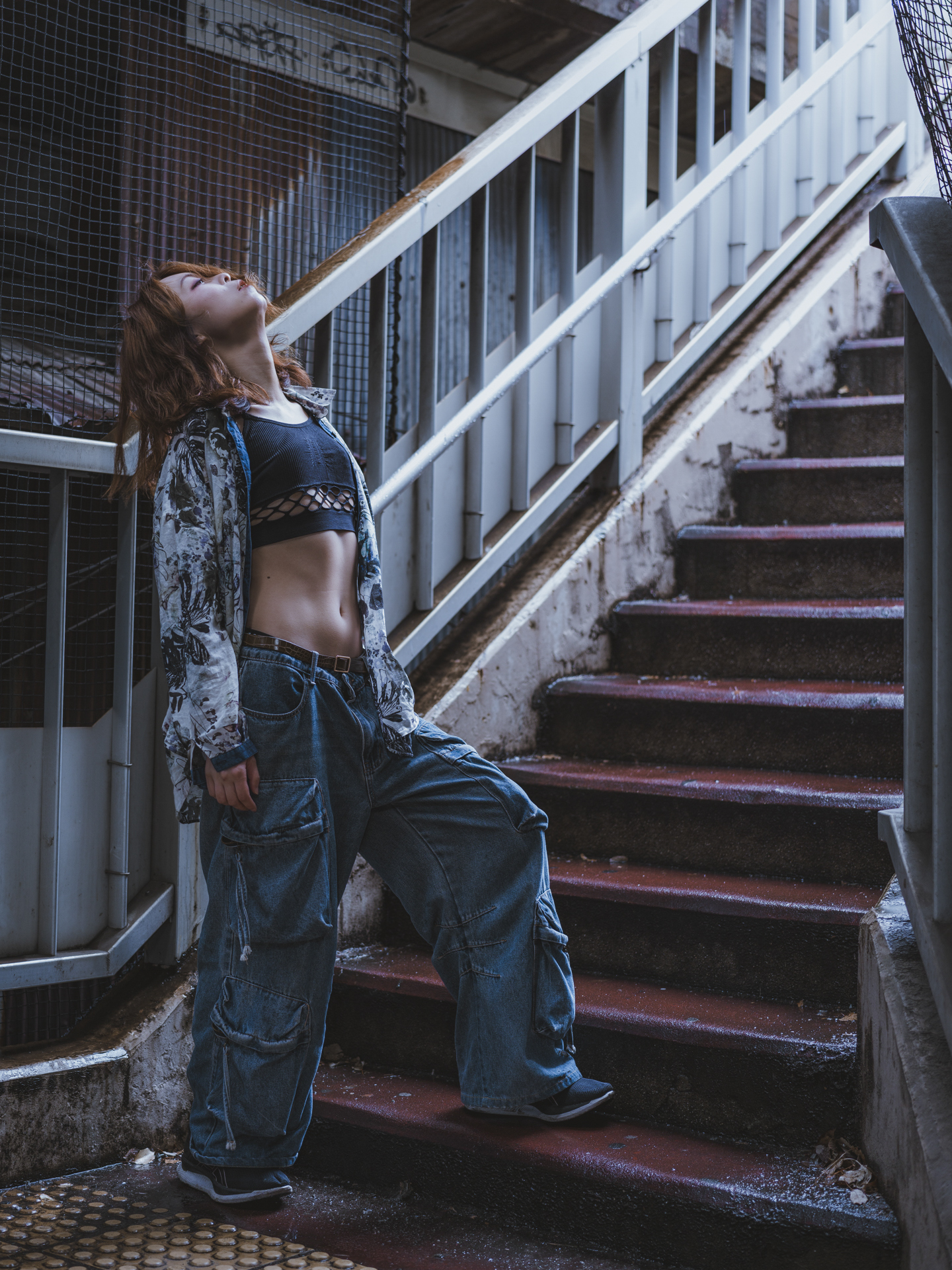 Japanese model Koishi showcasing personal street style wardrobe choices within a moody, industrial urban landscape during a rainy-day fashion editorial around Hankyu Nakatsu Station in Osaka.