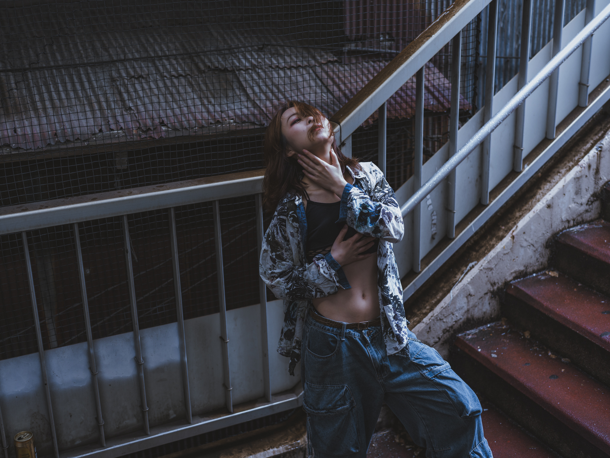 Japanese model Koishi showcasing personal street style wardrobe choices within a moody, industrial urban landscape during a rainy-day fashion editorial around Hankyu Nakatsu Station in Osaka.