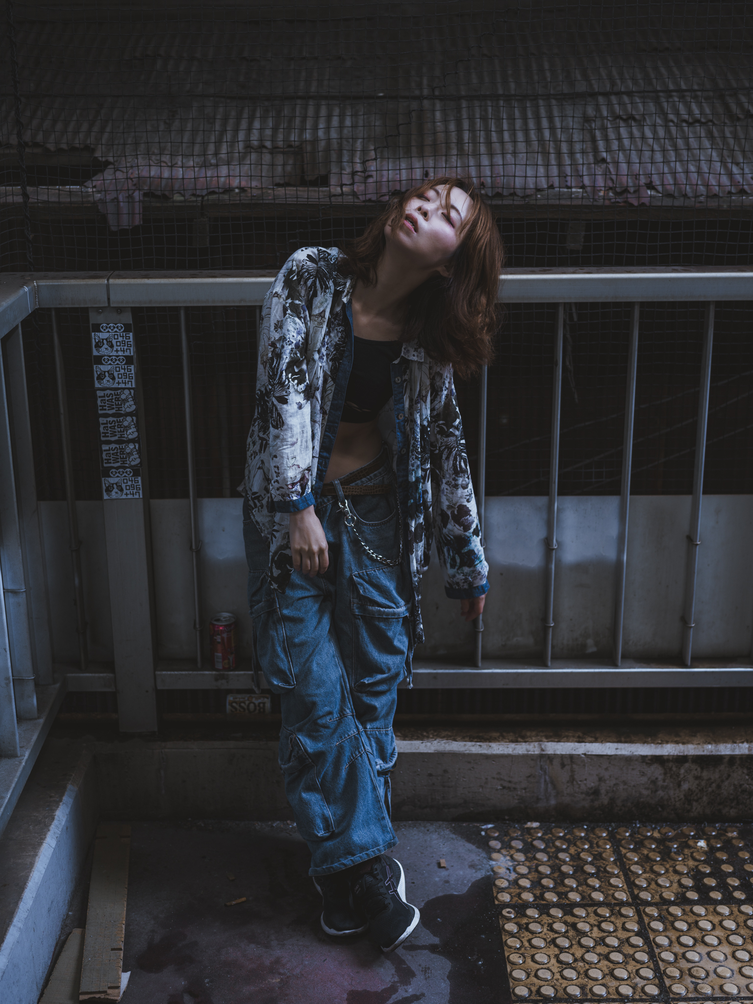 Japanese model Koishi showcasing personal street style wardrobe choices within a moody, industrial urban landscape during a rainy-day fashion editorial around Hankyu Nakatsu Station in Osaka.