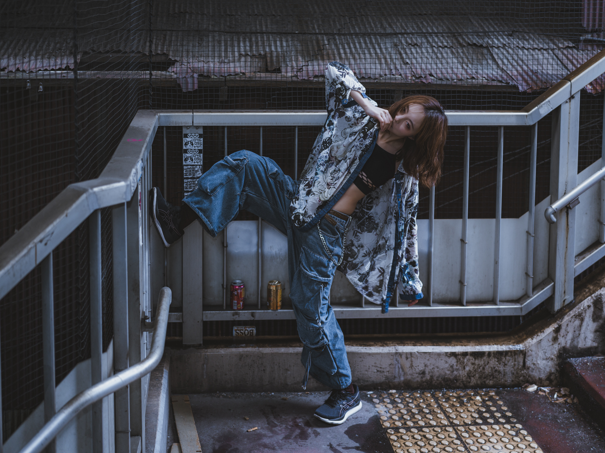 Japanese model Koishi showcasing personal street style wardrobe choices within a moody, industrial urban landscape during a rainy-day fashion editorial around Hankyu Nakatsu Station in Osaka.